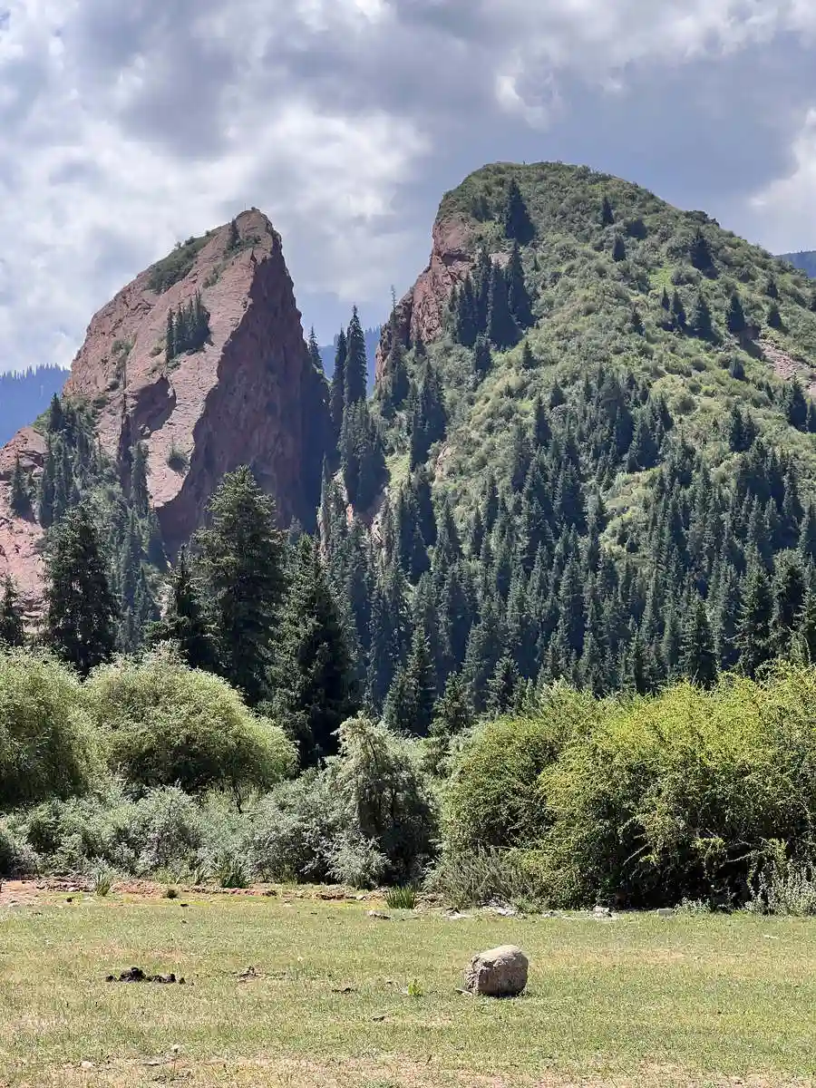 Red rock peak of the Jeti-Oguz 'Seven Bulls' formation rising above a green forested gorge